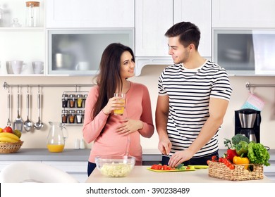 Pregnant Woman With Husband Cooking Food In Kitchen