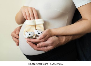 Pregnant woman with husband holding baby shoes on white bachground,closeup.Small shoes for the unborn baby. Pregnant couple.
