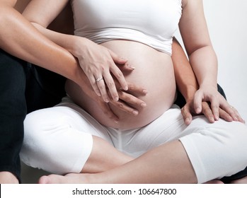 Pregnant woman with husband sitting on floor, holding hands on belly