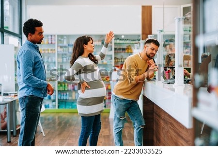 A pregnant woman is impatient and angry in a pharmacy queue annoyed with a customer ahead of her taking to long to finish shopping  with the pharmacist.