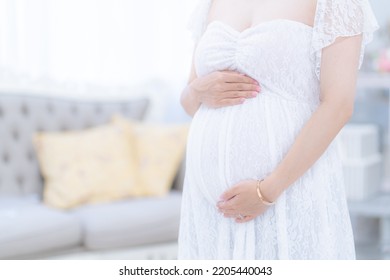 Pregnant Woman Indoors With Hands On Her Stomach In A Maternity Dress (shooting A Real Pregnant Woman)