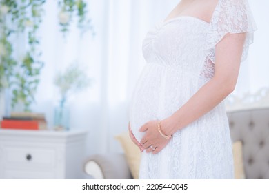 Pregnant Woman Indoors With Hands On Her Stomach In A Maternity Dress (shooting A Real Pregnant Woman)