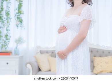 Pregnant Woman Indoors With Hands On Her Stomach In A Maternity Dress (shooting A Real Pregnant Woman)