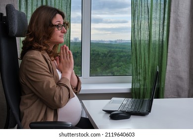 A pregnant woman with a laptop in her home office clasped her hands in prayer