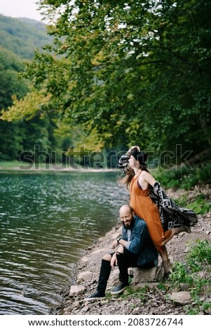 Pregnant woman leaning against a sitting laughing man on the lake