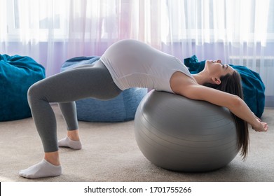 A pregnant woman lies with her back on a fitness ball. A woman in the third trimester goes in for sports. Pilates for expectant mothers.