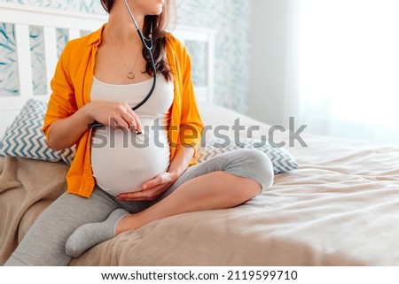 Pregnant woman listening to baby's heartbeat with stethoscope
