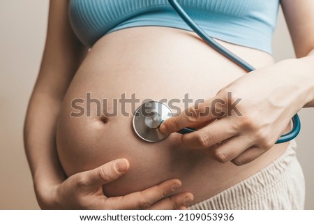 Pregnant woman listens to the baby heartbeat and movements with a stethoscope or fetoscope or Pinard Horn. Prenatal fetal health, anxiety, fear concept
