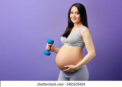 Pregnant Woman With Long Black Hair, Dressed In Crop Top Practicing Dumbbells In Purple Studio