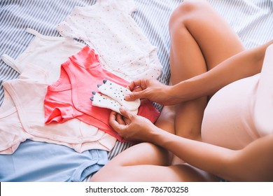 Pregnant woman looking of baby clothes. Young mother waiting of a baby. - Powered by Shutterstock