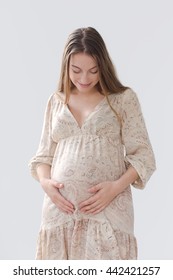 Pregnant woman looking at belly and strokes in a bright dress with long blond hair on white background