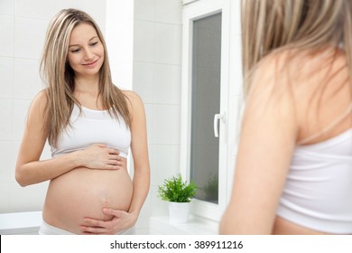Pregnant woman in looking into bathroom mirror