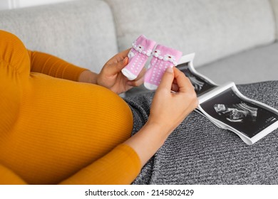 Pregnant woman looking at ultrasound scan gender reveal showing its a baby girl holding newborn pink socks awaiting the birth of her child. First trimester pregnancy