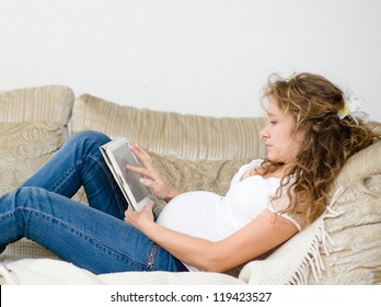 Pregnant Woman Lying Down On Sofa And Reading Ebook