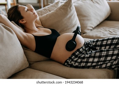 Pregnant woman lying on sofa at home with wireless headphones on belly. Baby in womb listening to music. - Powered by Shutterstock