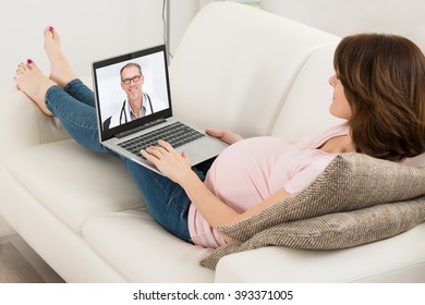 Pregnant Woman Lying On Sofa Videoconferencing With Doctor On Laptop - Powered by Shutterstock