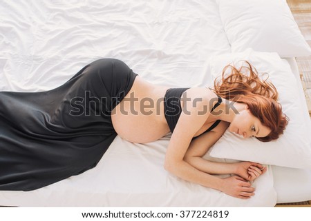 Pregnant woman lying on the white sheet thoughtfully