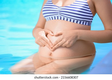 Pregnant Woman Making Heart Shape On Her Belly With Hands In Swimming Pool