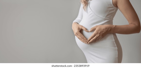 Pregnant woman making heart shape on stomach, Young pregnant woman doing heart gesture on belly - Powered by Shutterstock