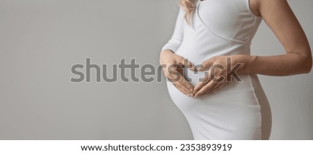 Pregnant woman making heart shape on stomach, Young pregnant woman doing heart gesture on belly