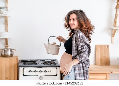 A Pregnant Woman Is Making Tea In The Kitchen, Holding A Kettle