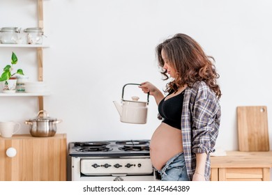 A Pregnant Woman Is Making Tea In The Kitchen, Holding A Kettle