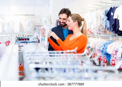 Pregnant Woman And Man Buying Baby Clothes In Store