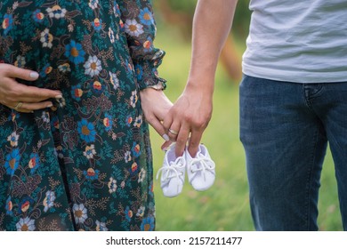 pregnant woman and man holding hands and holding baby shoes