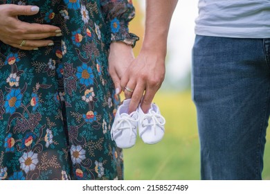 pregnant woman and man holding hands and holding baby shoes outdoors. pregnancy