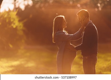 Pregnant woman and man posing at autumn park