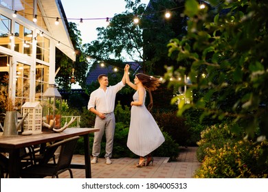 a pregnant woman and a man in smart clothes is dancing in the evening in garden in a country house by the fireplace. romantic relationships in the family.