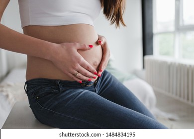 Pregnant woman with manicured hands on her belly. Heart shaped hands. Expecting a baby and happy maternity concept .Big belly on third trimester of pregnancy close-up. 