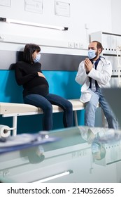 Pregnant Woman And Medic Doing Examination During Covid 19 Pandemic. Patient Talking To Doctor With Face Mask About Pregnancy And Childbirth, Specialist Giving Medical Advice In Office.