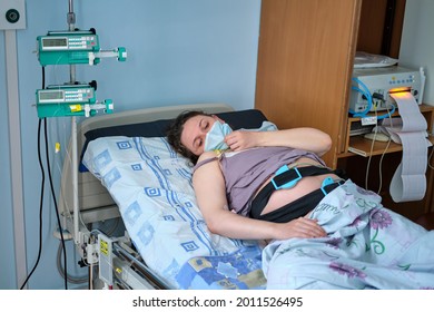 A pregnant woman in medical mask gives birth in a hospital with a drip and a CTG machine. A woman on a clinic bed during labor pains.