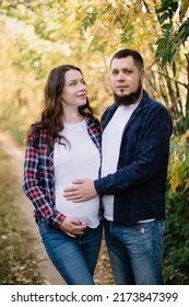 Pregnant Woman, Mom-to-be, Stands Next To Dad In The Autumn Forest And Hugs. Gently Touch By Hand Of The Stomach With The Future Child. Pregnancy, Love. High Quality Shot.