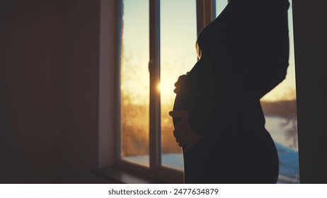 pregnant woman. motherhood pregnancy concept light. 40 year old pregnant woman stands in a dress by the window holding her stomach silhouette. silhouette of a girl in at sunset by the window - Powered by Shutterstock