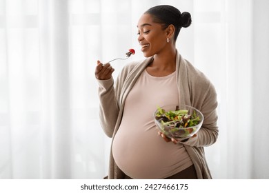 Pregnant Woman Nutrition. Happy Black Expecting Lady Eating Fresh Vegetable Salad While Standing Next To Window, Enjoying Healthy Organic Food During Pregnancy, Copy Space - Powered by Shutterstock