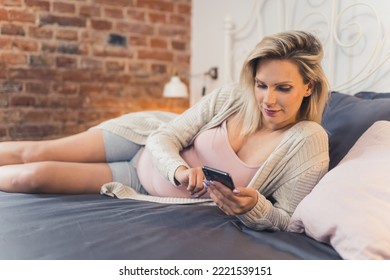 Pregnant Woman On The Bed Scrolling Social Media. High Quality Photo