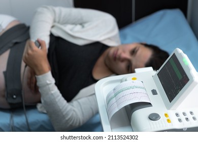 Pregnant Woman On Hospital Couch During Medical Control Cardiotocography. Gynecologist Doctor Hands Turn On Adjust CTG Device Clinic Consultant. Examine Expectant Belly Baby Mother Healthcare Check Up