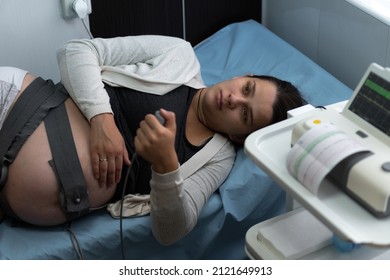 Pregnant Woman On Hospital Couch During Medical Control Cardiotocography. Gynecologist Doctor Hands Turn On Adjust CTG Device Clinic Consultant. Examine Expectant Belly Baby Mother Healthcare Check Up