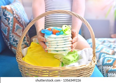 Pregnant Woman Packing Bag For Maternity Hospital At Home. Preparing For Newborn Birth. Future Mom Holding Stack Of Diapers Above The Basket. 