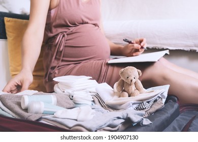 Pregnant Woman Packing Bag For Maternity Hospital, Making Notes, Checking List In Diary. Expectant Mother With Suitcase Of Baby Clothes And Necessities Preparing For Newborn Birth During Pregnancy.