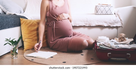 Pregnant Woman Packing Bag For Maternity Hospital, Making Notes, Checking List In Diary. Expectant Mother With Suitcase Of Baby Clothes And Necessities Preparing For Newborn Birth During Pregnancy.