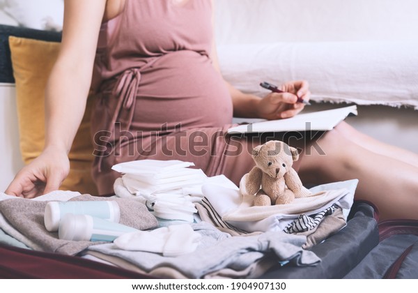 Pregnant woman packing bag for maternity\
hospital, making notes, checking list in diary. Expectant mother\
with suitcase of baby clothes and necessities preparing for newborn\
birth during\
pregnancy.