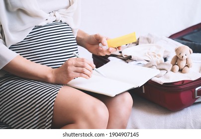 Pregnant woman packing hospital bag with checklist. Expectant mother with travel suitcase of baby clothes and necessities preparing for newborn birth, labor, making notes in paper diary. - Powered by Shutterstock