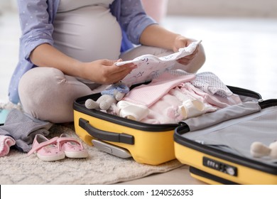 Pregnant woman packing suitcase for maternity hospital at home, closeup