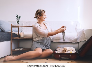 Pregnant woman is packing suitcase for maternity hospital getting ready for childbirth. Happy young mother with travel luggage of baby clothes at home. Preparation for newborn birth during pregnancy. - Powered by Shutterstock