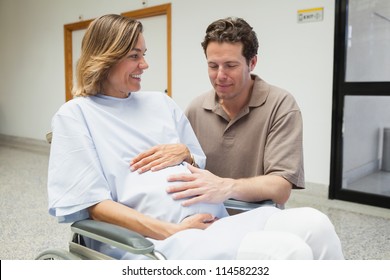 Pregnant woman and partner both touching her belly and smiling in hospital corridor, Healthcare workers in the Coronavirus Covid19 pandemic - Powered by Shutterstock