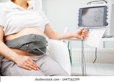 Pregnant woman performing cardiotocography (CTG). The belt on her belly connected to the Cardiotocograph machine aka Electronic Fetal Monitor (EFM) recording the fetal heartbeat 