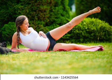 Pregnant Woman Performing Side Reclining Leg Lift In Park